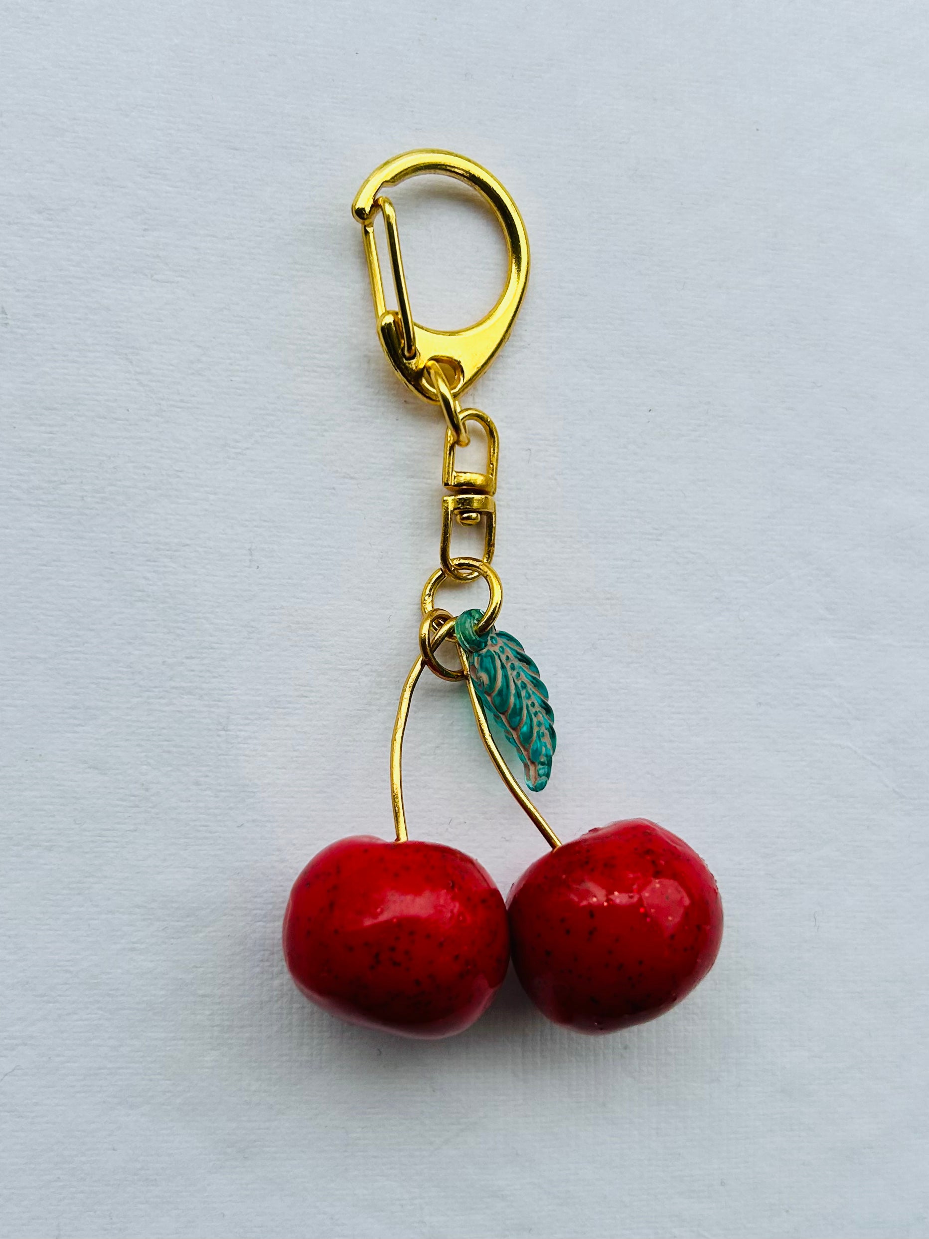 Cherry charm keychain for women: two red polymer cherries, epoxy shine, green glass leaf, on a gold-plated clasp chain.