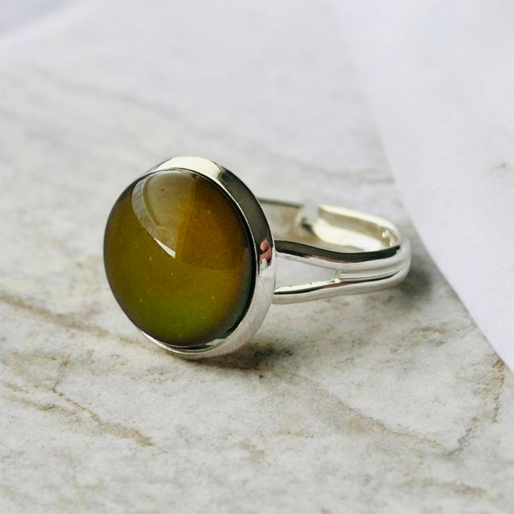 Mood Ring with brown oval stone on a silver band resting on marble.