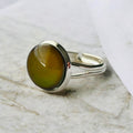 Mood Ring with brown oval stone on a silver band resting on marble.